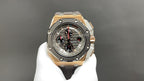 Octagonal luxury watch with dark dial, gold-tone bezel, and gray rubber strap