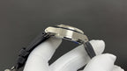 Stainless steel watch case with black rubber strap, side view.
