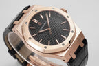 Audemars Piguet watch close-up with rose gold case, black dial, and black leather strap.