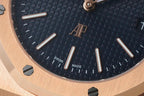 Dark blue wristwatch dial close-up with baton hour markers and logo at center.