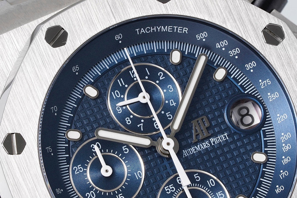 Blue chronograph dial close-up with tachymeter ring, subdials, and white indices