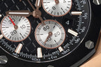 Audemars Piguet watch dial close-up, black face with white subdials and red accents.
