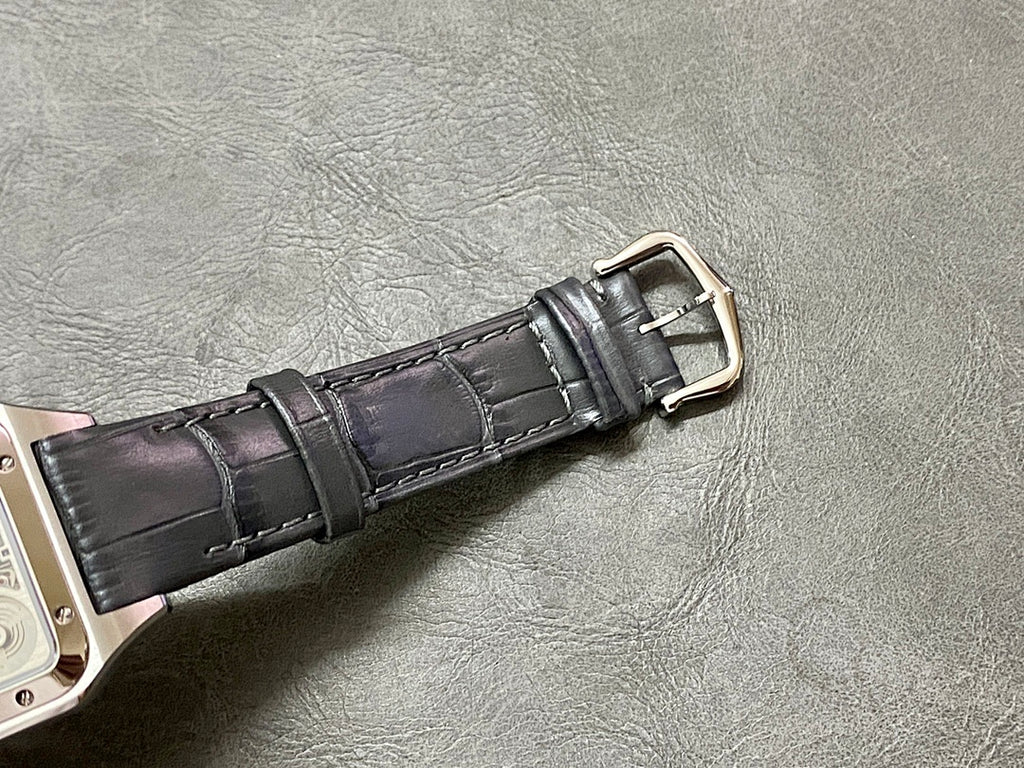 Black leather watch strap with silver-tone buckle connected to a square case