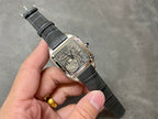 Square skeleton watch on black leather strap held in hand; silver-tone case visible