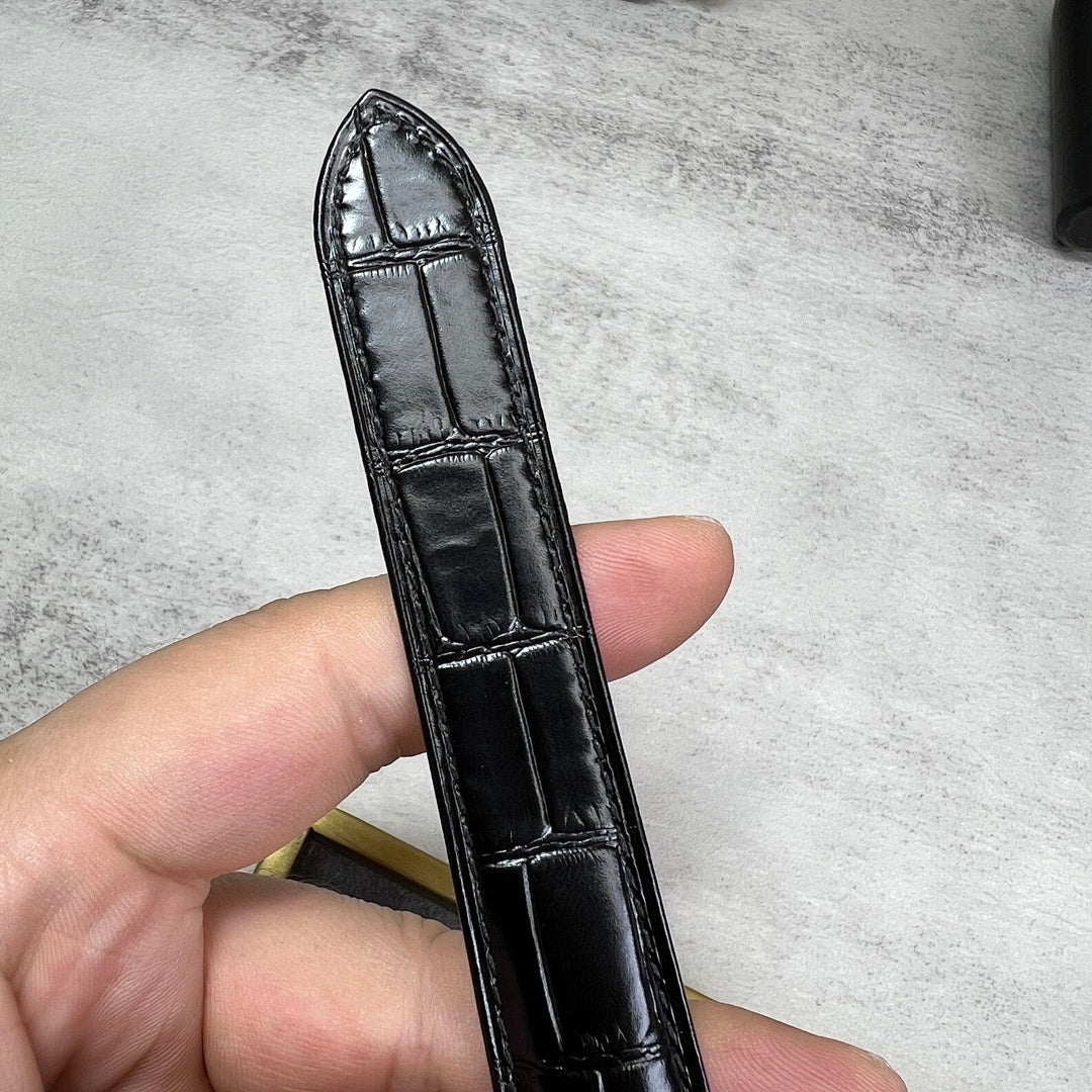 Black leather watch strap with stitched edges and folding keeper; strap underside visible.