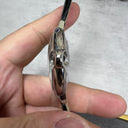 Silver-tone watch case side with crown tube and black leather strap; polished curves.