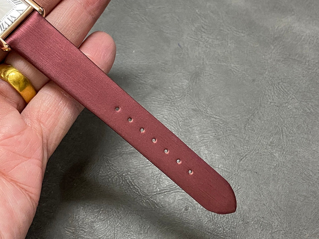 Burgundy leather watch strap with multiple holes, held in hand