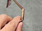 Gold-toned watch case and burgundy leather strap, side view with crown area