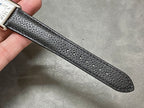 Black leather watch strap, textured grain, single straight band with stitched edge.