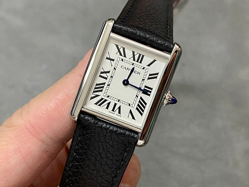 Cartier watch with black leather strap, rectangular silver case, white dial, Roman numerals.