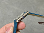 Silver watch case with blue stone detail and blue leather strap.