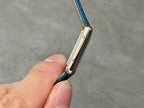 Silver watch case with crown hardware and blue leather strap loop.