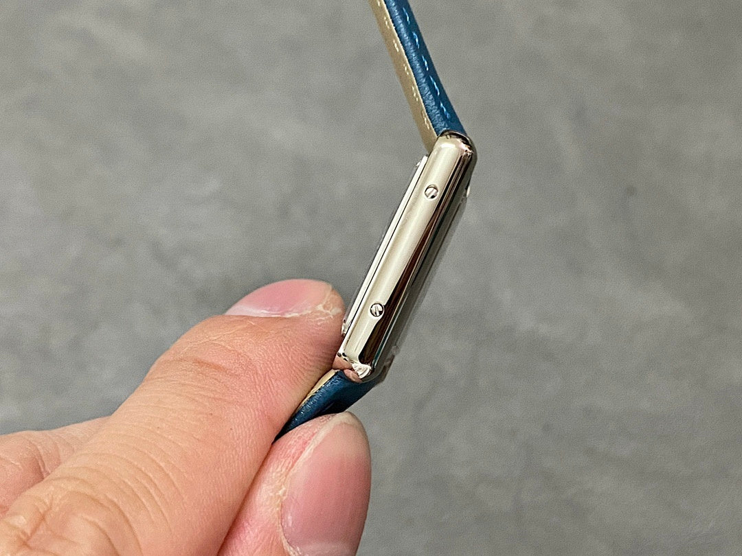 Silver watch case with crown hardware and blue leather strap loop.