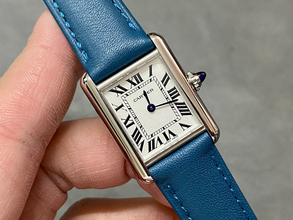 Square silver wristwatch with Roman numeral dial and blue leather strap close-up.