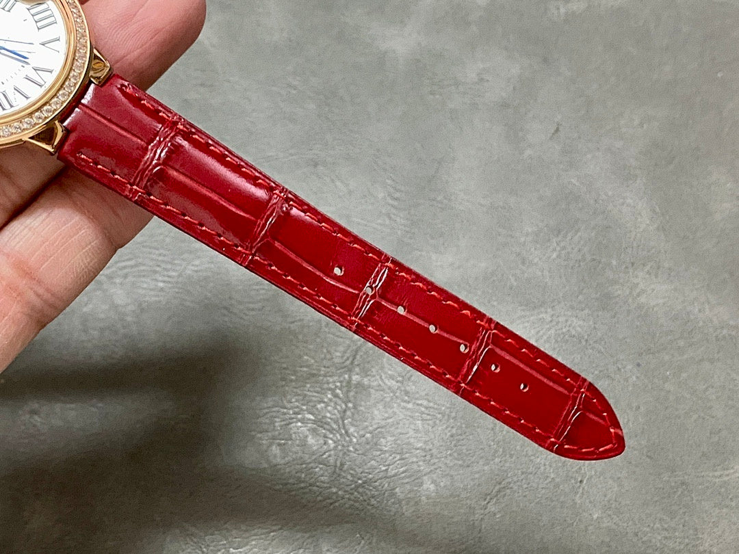 Red leather watch strap with gold-tone clasp ends and stitched texture