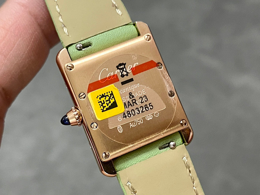 Gold-tone watch caseback on green leather strap with QR label and serial text
