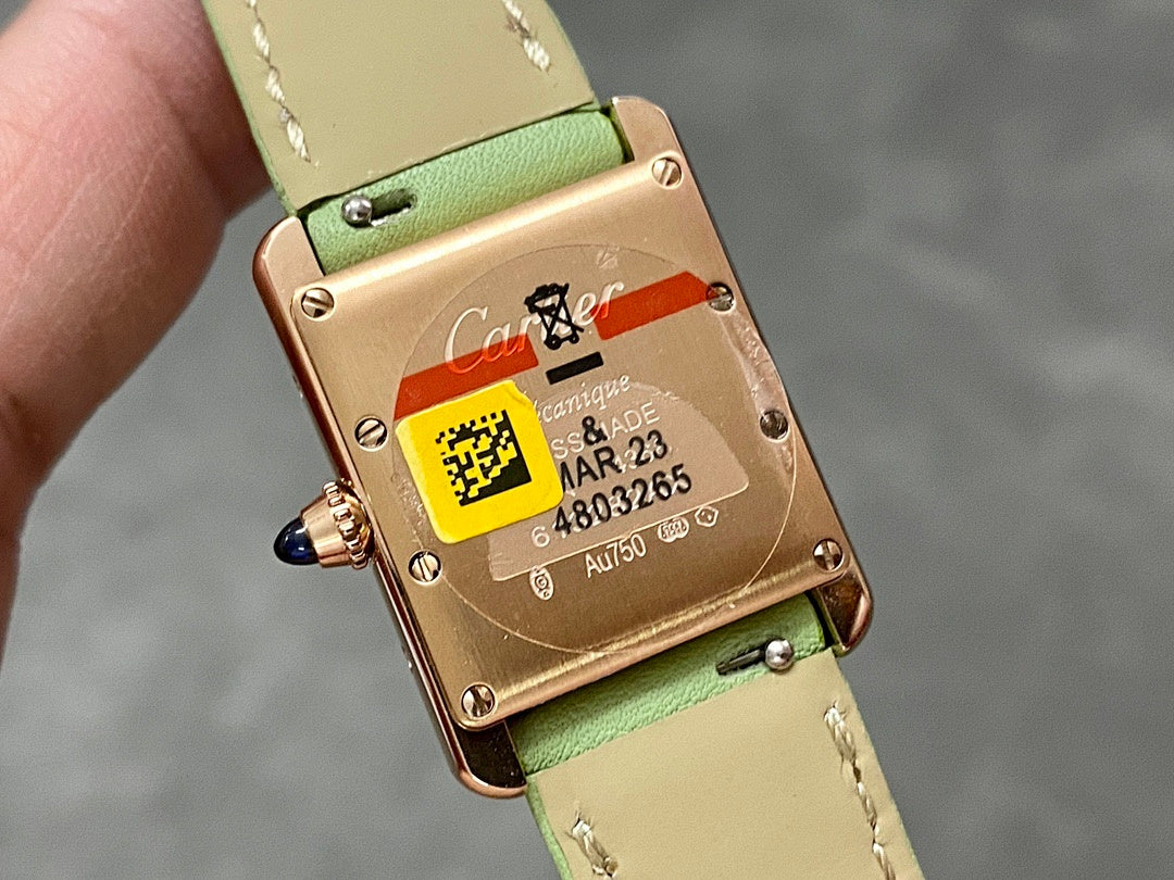 Gold-tone watch caseback on green leather strap with QR label and serial text