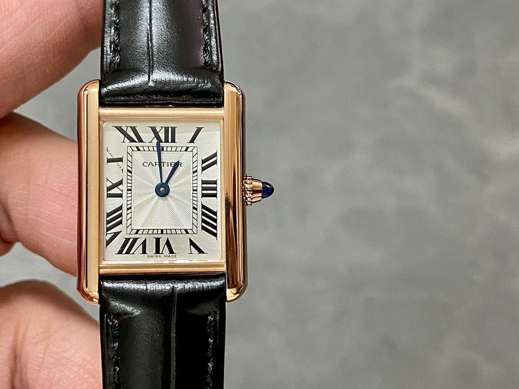 Cartier watch front close-up: black leather strap, gold-toned case, white dial, Roman numerals