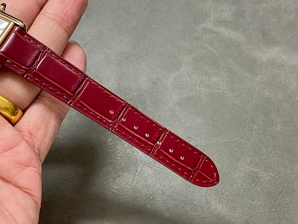 Burgundy leather watch strap with gold-tone case edge and crocodile-style texture