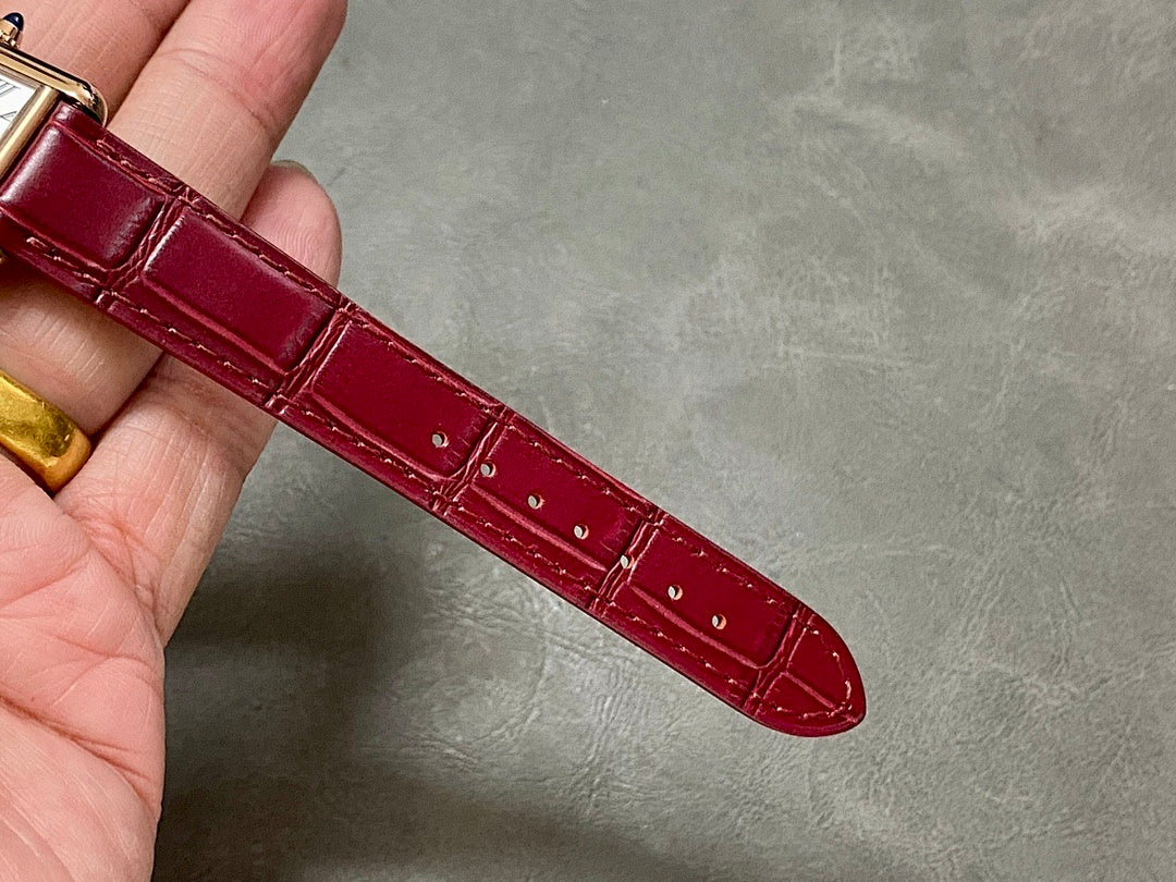 Burgundy leather watch strap with gold-tone case edge and crocodile-style texture