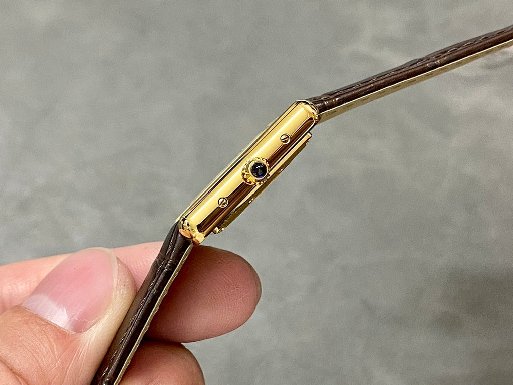 Cartier watch side view with gold crown and blue gem, brown leather strap