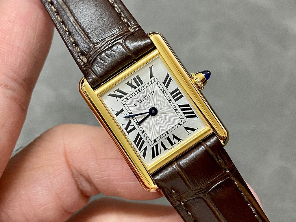 Cartier watch held in hand, gold case, white dial with Roman numerals, brown leather strap