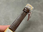 Rectangular wristwatch with brown leather strap and gold-tone case, tag attached at buckle