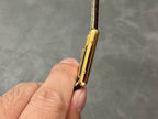 Gold-tone rectangular wristwatch case from a side angle with brown leather strap
