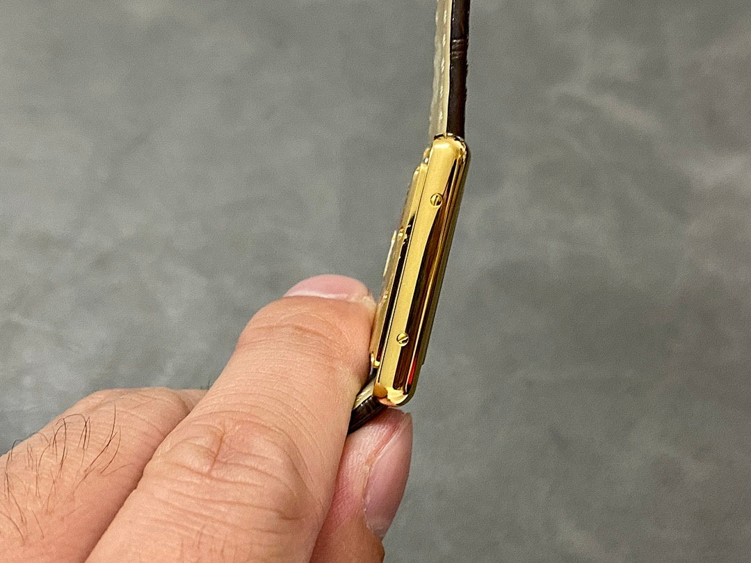 Gold-tone rectangular wristwatch case from a side angle with brown leather strap
