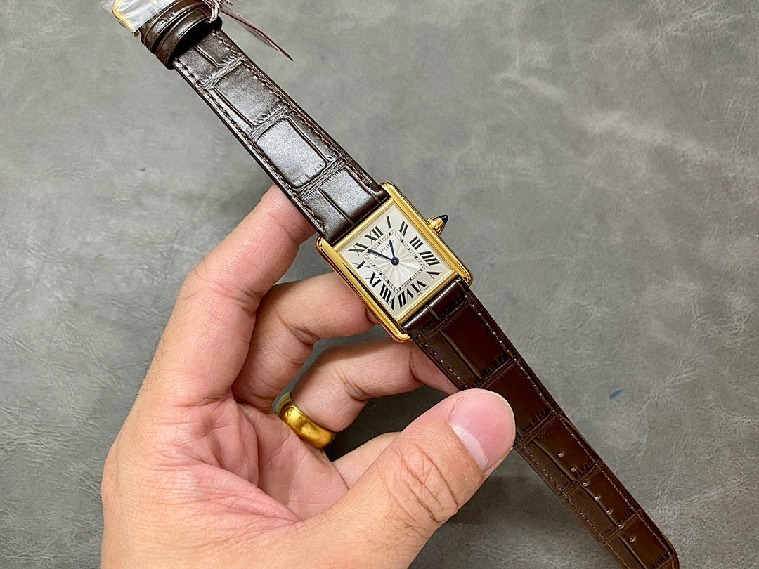 Rectangular wristwatch with Roman numeral dial, gold-tone case, and brown leather strap in hand