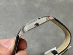 Cartier watch side view; silver case with blue gemstone crown, black leather strap.