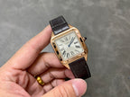 Cartier watch on hand with gold-tone square case, white dial, Roman numerals, black leather strap