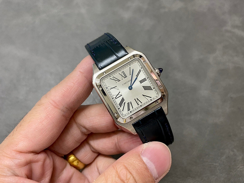 Cartier watch held in hand with black leather strap, square silver case, Roman dial.