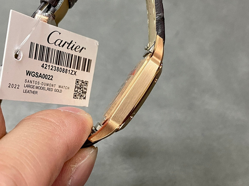 Wristwatch with black leather strap and tag showing barcode, gold-tone case.