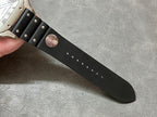 Black leather watch strap with stud details and engraved circular stamp near buckle end