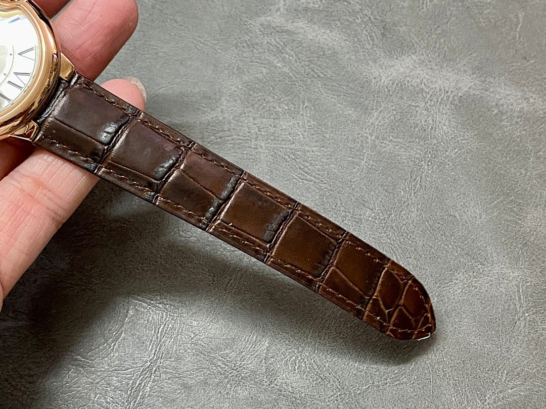 Brown leather watch strap with stitched edges and buckle, laid across the hand