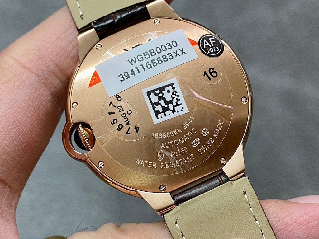 Rose-gold watch caseback with labels and QR code, on light brown leather strap