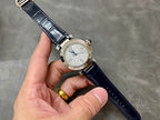 Cartier wristwatch on wrist with silver dial, dark blue leather strap, and metal buckle.