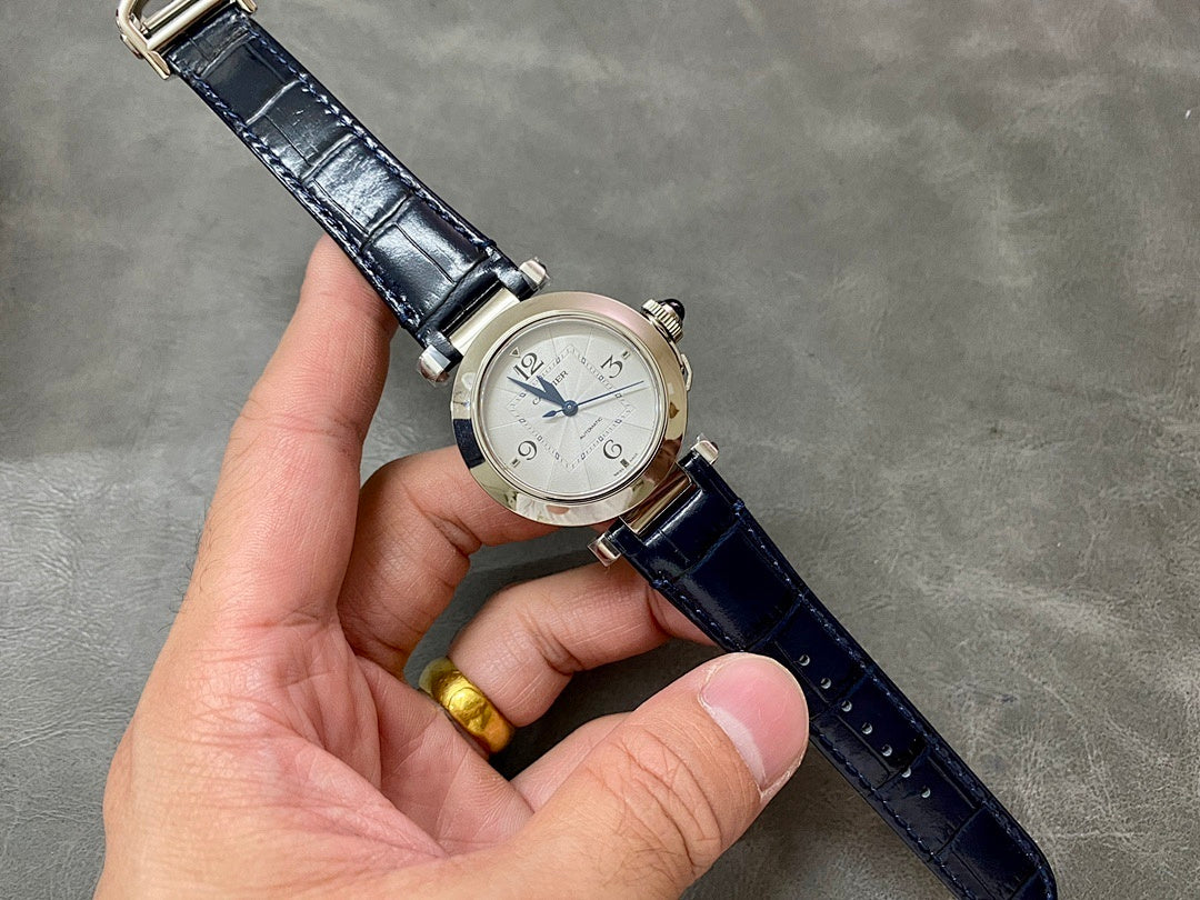 Cartier wristwatch on wrist with silver dial, dark blue leather strap, and metal buckle.