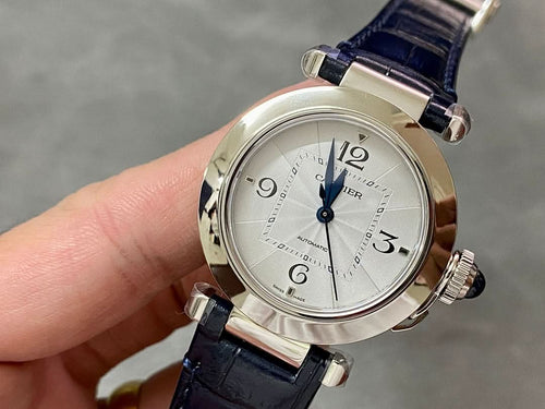 Cartier wristwatch with silver dial and dark blue leather strap, held in hand.