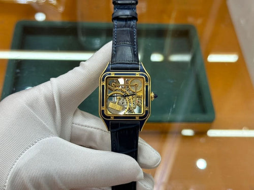 Gold-tone wristwatch with black leather strap and square skeleton dial, held in hand