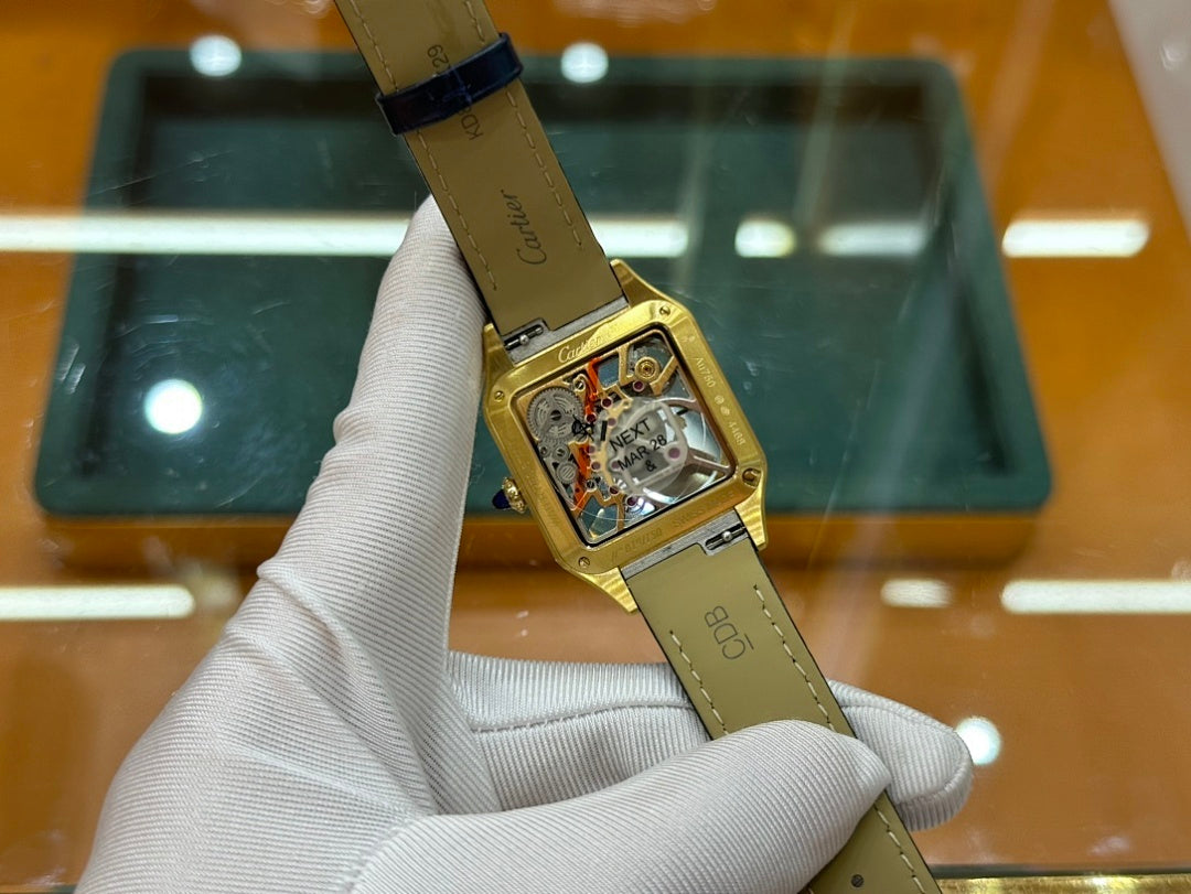 Gold-tone wristwatch with black leather strap and open-work dial, held angled