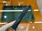 Gold-tone wristwatch with black leather strap, angled view of strap and case