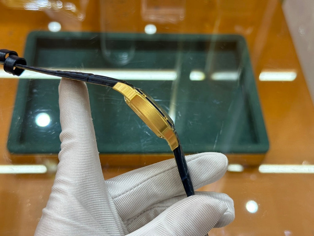 Gold-tone wristwatch with black leather strap, shown from side with case edge