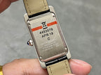 Rectangular watch case back with engraved markings and black leather strap with tan stitching.
