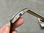 Rectangular wristwatch case edge with blue gem set on bezel, black leather strap.