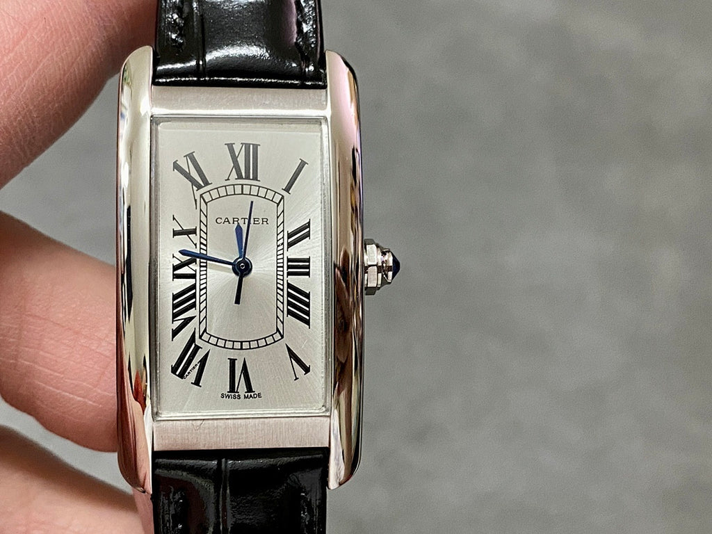 Rectangular wristwatch with silver-tone case, white dial and blue hands, black leather strap.