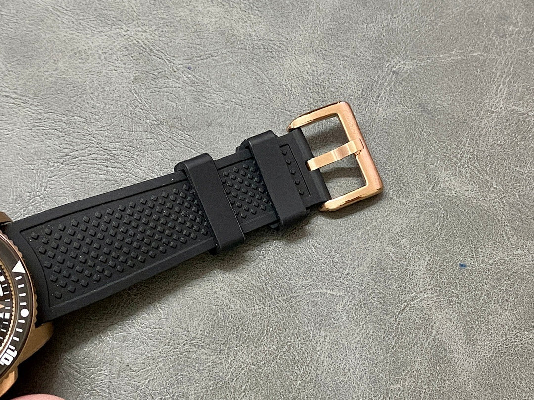 Black rubber watch strap with rose-gold buckle and keeper loop