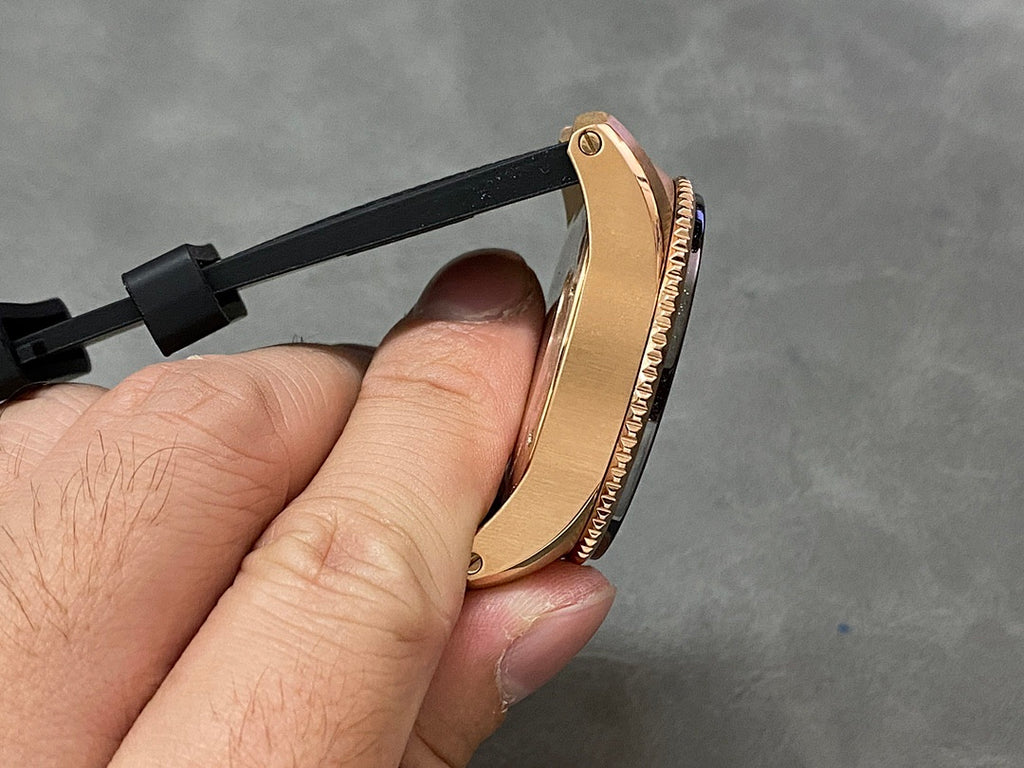 Gold-tone watch side view with black rubber strap and ridged bezel edge