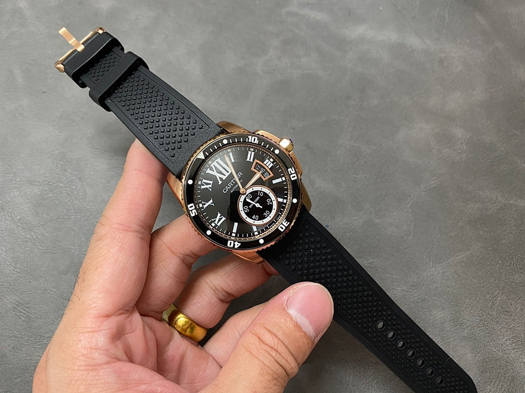 Gold-tone dive watch with black dial and textured black strap, held in hand